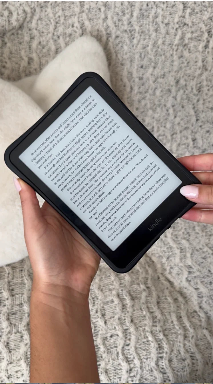Hand holding Kindle with black electronic case, reading on textured blanket background